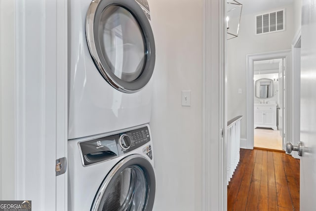 laundry area featuring stacked washing maching and dryer, laundry area, visible vents, and dark wood-style flooring