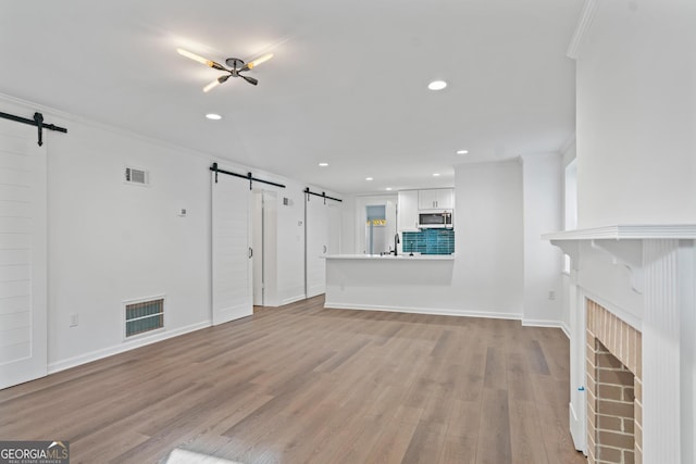 unfurnished living room with a barn door, a brick fireplace, visible vents, and light wood-style floors