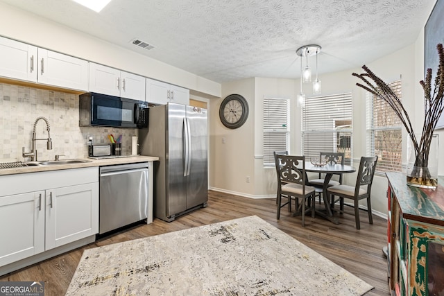 kitchen featuring stainless steel appliances, wood finished floors, a sink, visible vents, and tasteful backsplash