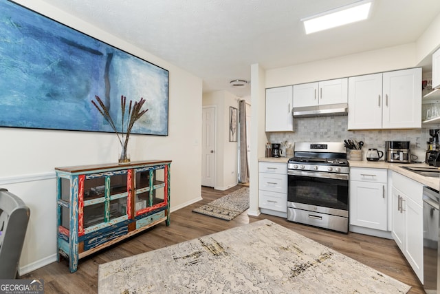 kitchen with stainless steel appliances, decorative backsplash, white cabinets, wood finished floors, and under cabinet range hood