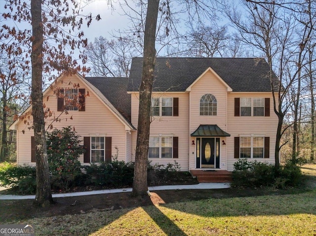 colonial inspired home featuring roof with shingles and a front yard