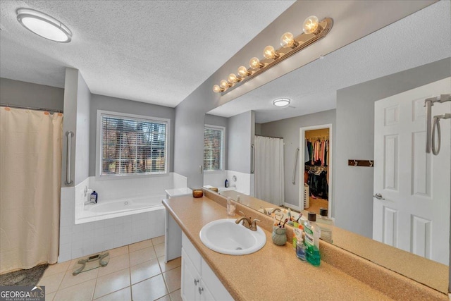 bathroom featuring a walk in closet, a garden tub, vanity, a textured ceiling, and tile patterned flooring