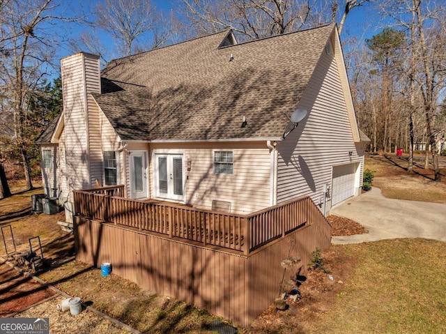 back of property with driveway, french doors, roof with shingles, and a chimney