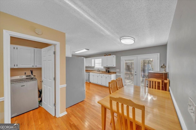 dining area with baseboards, light wood-style flooring, washer / clothes dryer, a textured ceiling, and french doors