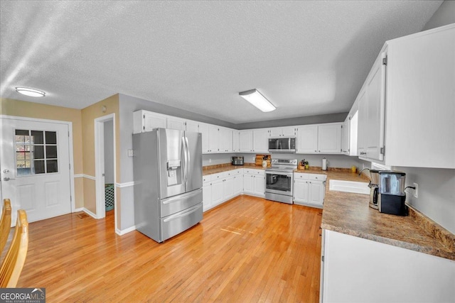 kitchen with white cabinets, stainless steel appliances, a textured ceiling, light wood-type flooring, and a sink