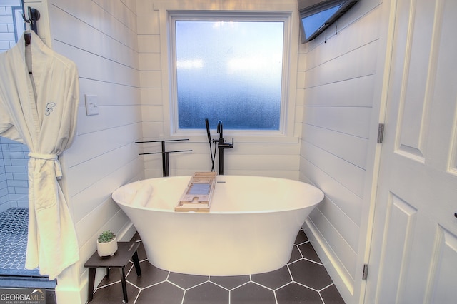 bathroom with wooden walls, a freestanding tub, and tile patterned floors