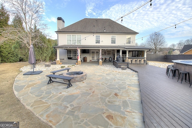 back of property with an outdoor fire pit, a shingled roof, a chimney, fence, and a deck