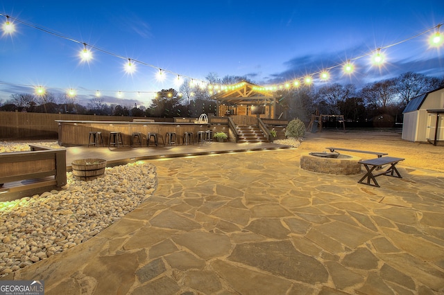 view of patio / terrace featuring an outbuilding, outdoor dry bar, fence, a shed, and a fire pit