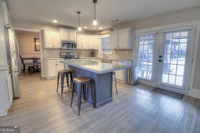 kitchen with white cabinets, stainless steel appliances, light countertops, a kitchen bar, and a sink