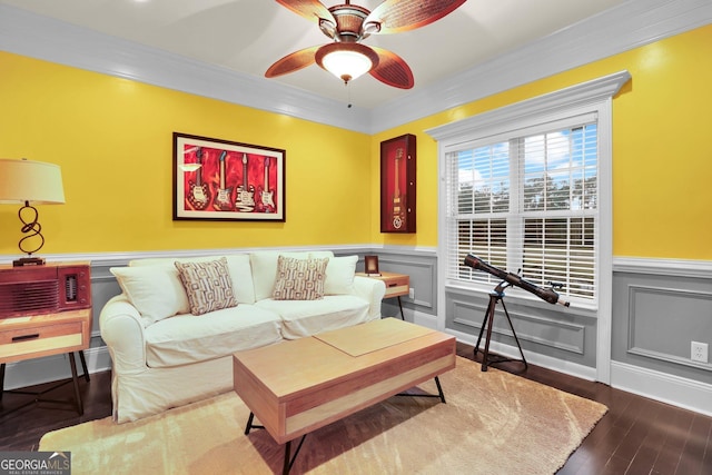 living area with ceiling fan, dark wood finished floors, crown molding, and wainscoting