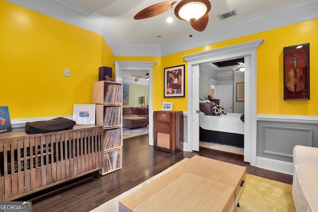 bedroom featuring ceiling fan, a wainscoted wall, wood finished floors, visible vents, and ornamental molding