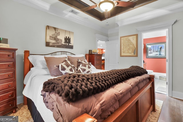 bedroom with baseboards, visible vents, a raised ceiling, ornamental molding, and light wood-style floors