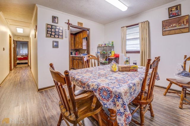 dining space with a textured ceiling, light wood-style floors, baseboards, and crown molding