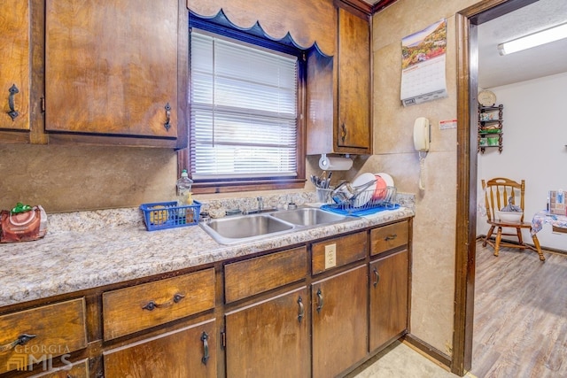 kitchen with brown cabinetry, light wood-style floors, light countertops, and a sink