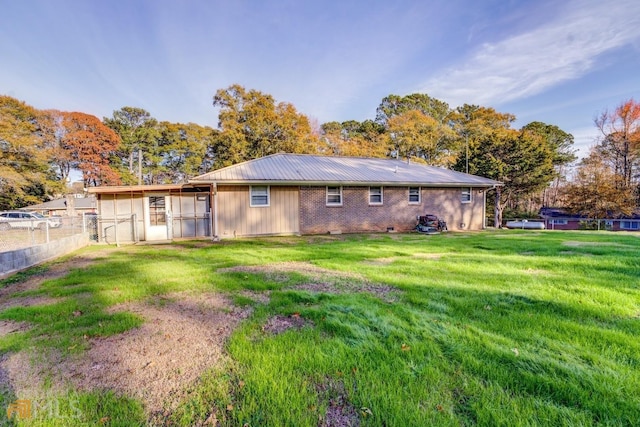 back of property featuring fence, metal roof, a lawn, and brick siding