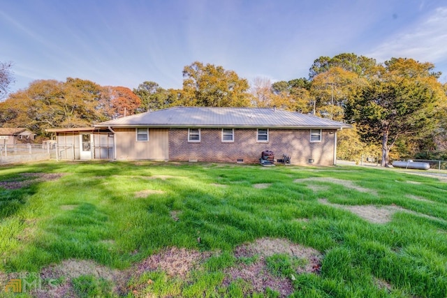 back of property with metal roof, brick siding, fence, a yard, and crawl space