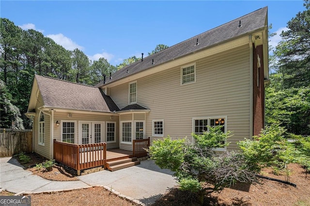 rear view of house with a wooden deck, roof with shingles, and french doors