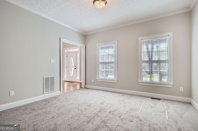 carpeted empty room with baseboards, a textured ceiling, visible vents, and crown molding