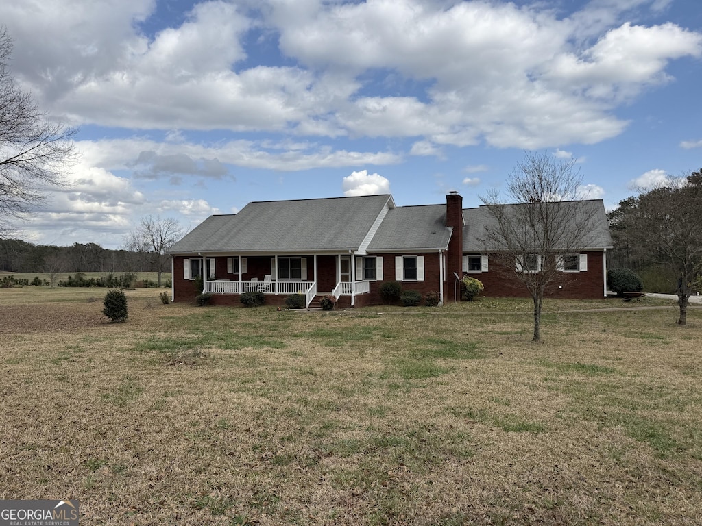 view of front facade featuring brick siding, a porch, a chimney, and a front yard