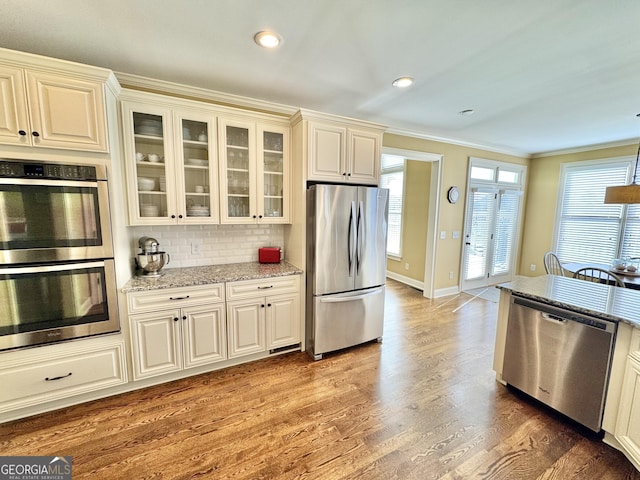 kitchen with light stone countertops, a wealth of natural light, stainless steel appliances, and wood finished floors