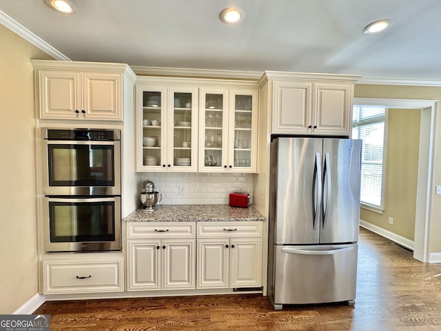 kitchen with dark wood finished floors, appliances with stainless steel finishes, light stone countertops, crown molding, and backsplash