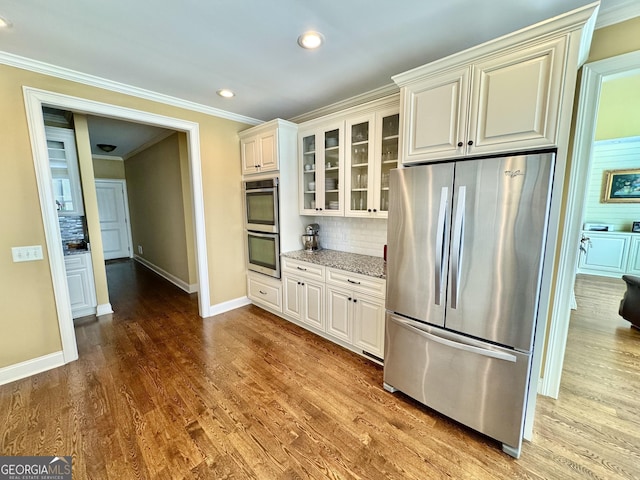 kitchen with light stone countertops, stainless steel appliances, wood finished floors, decorative backsplash, and crown molding