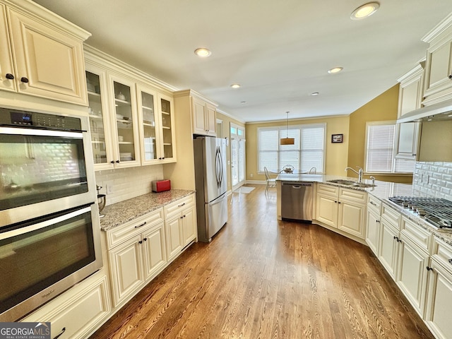 kitchen with glass insert cabinets, light stone counters, appliances with stainless steel finishes, dark wood-type flooring, and a sink