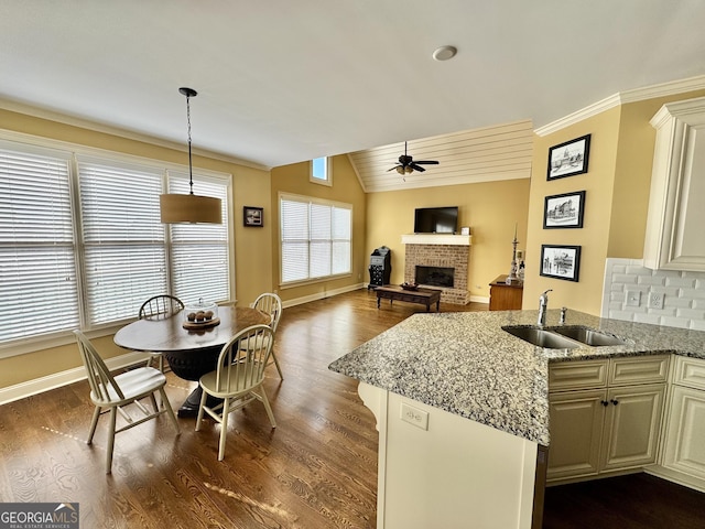 kitchen featuring dark wood finished floors, lofted ceiling, ceiling fan, a fireplace, and a sink