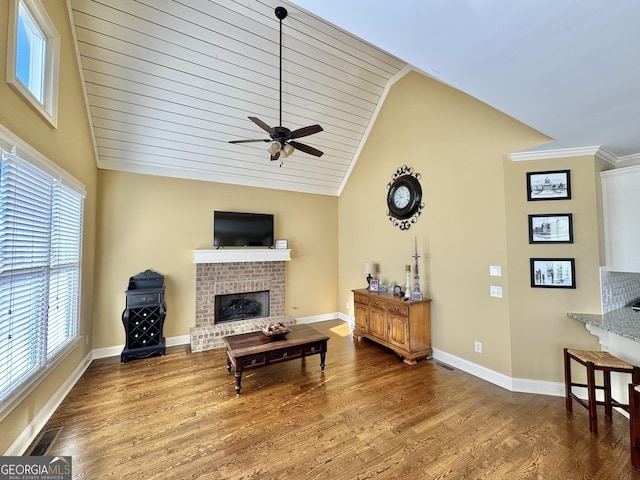 living room featuring baseboards, visible vents, wood finished floors, vaulted ceiling, and a fireplace