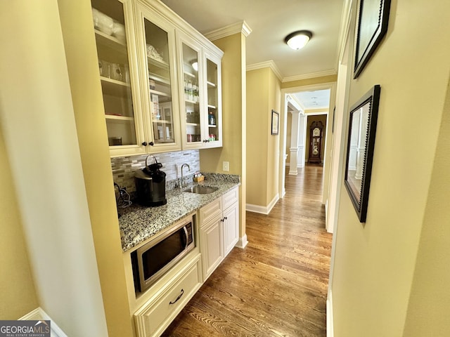 interior space featuring stainless steel microwave, wood finished floors, a sink, crown molding, and backsplash