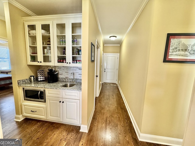 bar featuring dark wood-style floors, stainless steel microwave, backsplash, and a sink