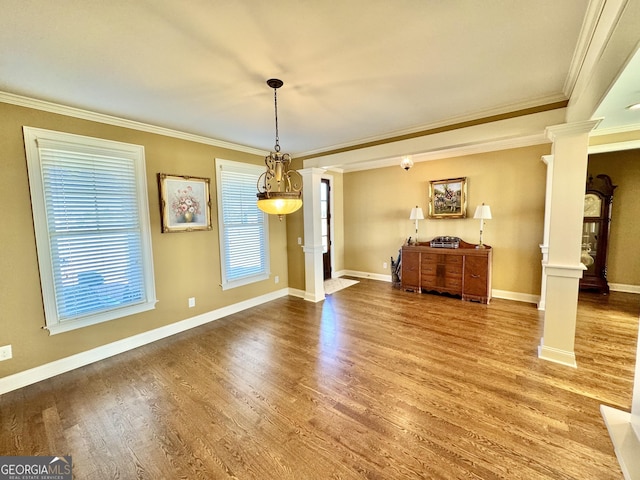 unfurnished dining area with ornate columns, crown molding, baseboards, and wood finished floors