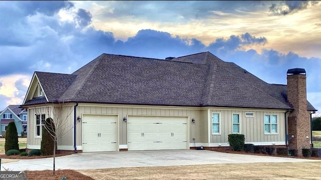 view of front of property featuring a garage, driveway, roof with shingles, board and batten siding, and a chimney