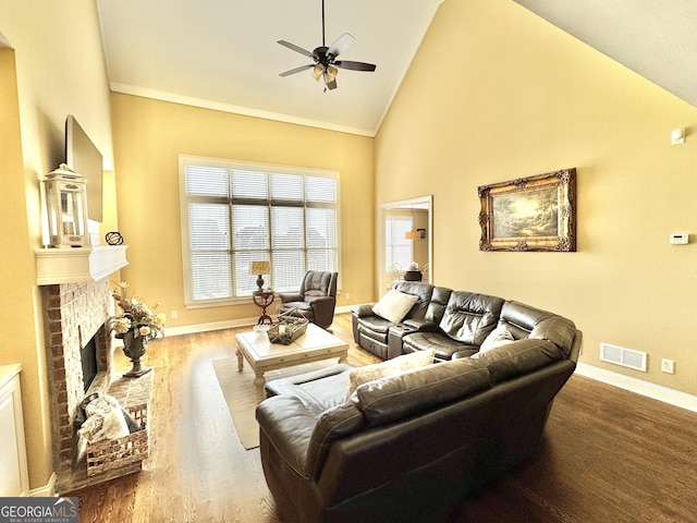 living room with visible vents, baseboards, wood finished floors, a brick fireplace, and high vaulted ceiling