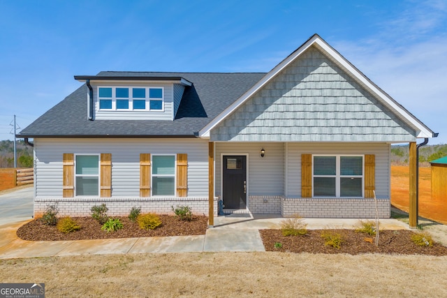 view of front of home featuring roof with shingles, a porch, and brick siding