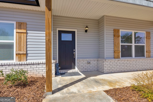 entrance to property featuring a porch and brick siding