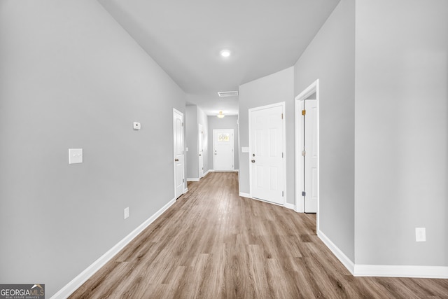 hallway with light wood finished floors, visible vents, and baseboards