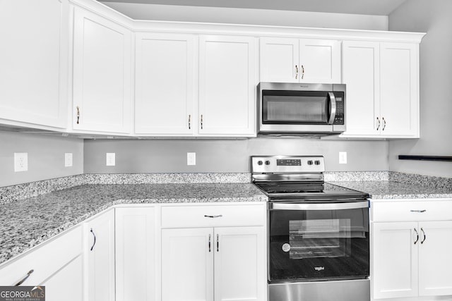 kitchen with stainless steel appliances, light stone counters, and white cabinetry