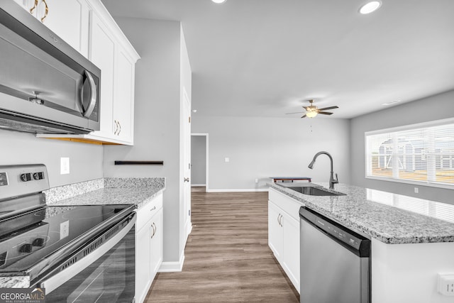 kitchen featuring wood finished floors, light stone countertops, stainless steel appliances, white cabinetry, and a sink