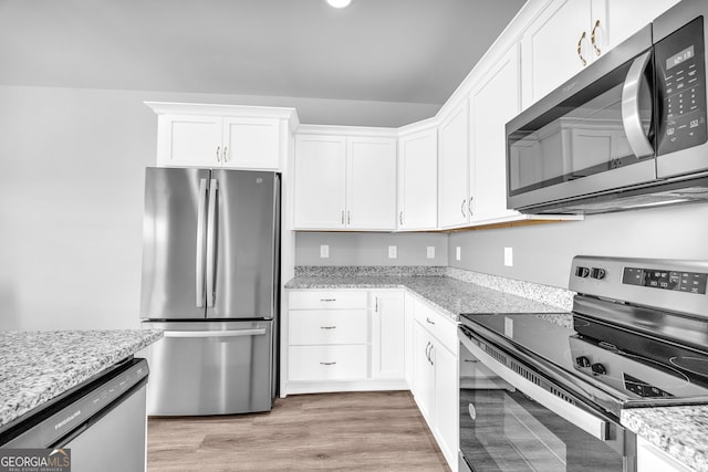 kitchen with stainless steel appliances, light stone counters, white cabinetry, and light wood-style floors