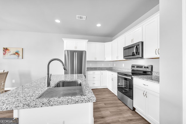 kitchen with visible vents, appliances with stainless steel finishes, a kitchen island with sink, white cabinets, and a sink