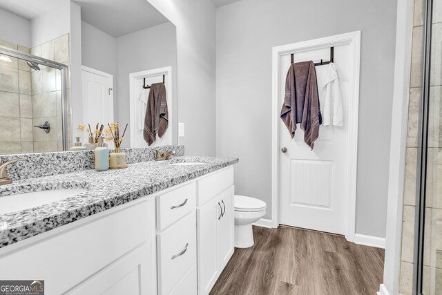 bathroom with double vanity, wood finished floors, a stall shower, and a sink