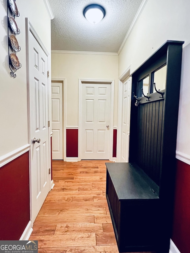 mudroom with a textured ceiling, ornamental molding, baseboards, and light wood-style floors