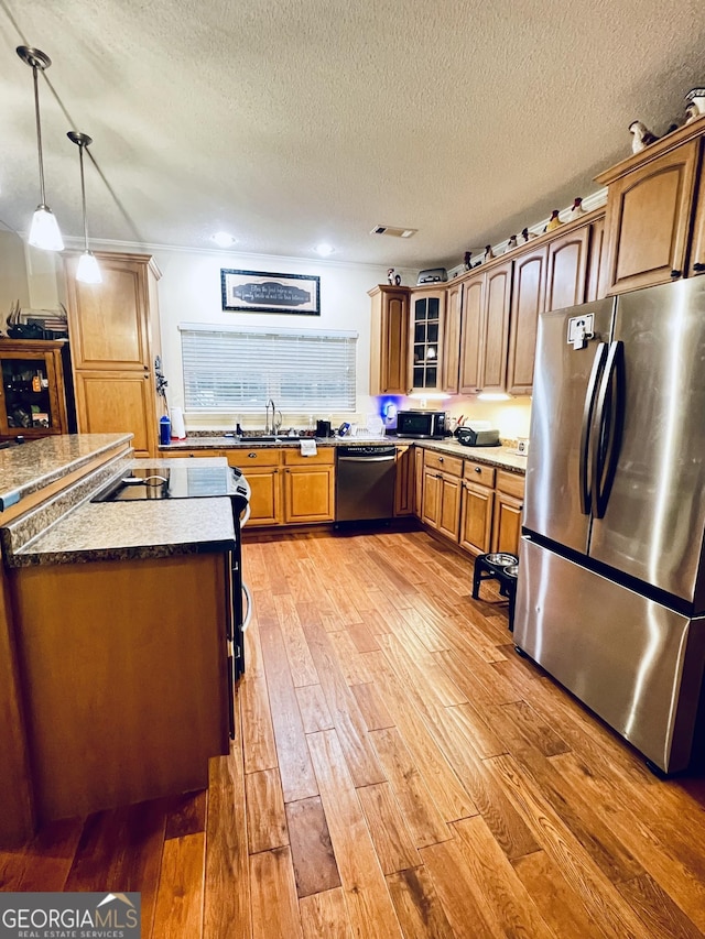 kitchen featuring stainless steel appliances, light wood-style flooring, brown cabinetry, glass insert cabinets, and a textured ceiling