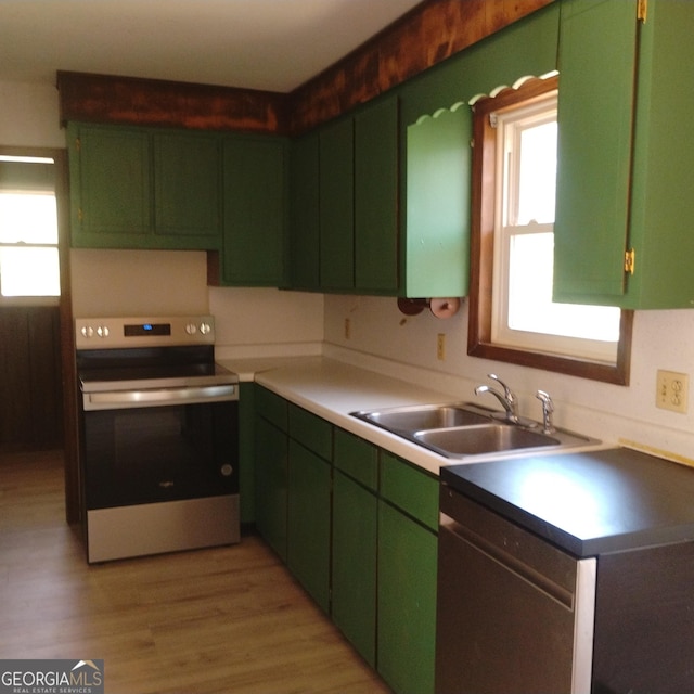 kitchen with a sink, light wood finished floors, stainless steel appliances, and green cabinetry