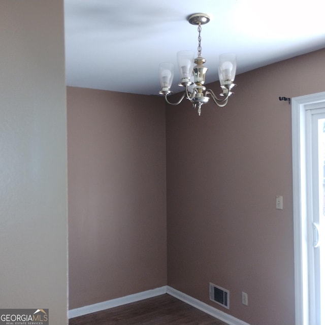 spare room featuring baseboards, visible vents, dark wood finished floors, and a notable chandelier