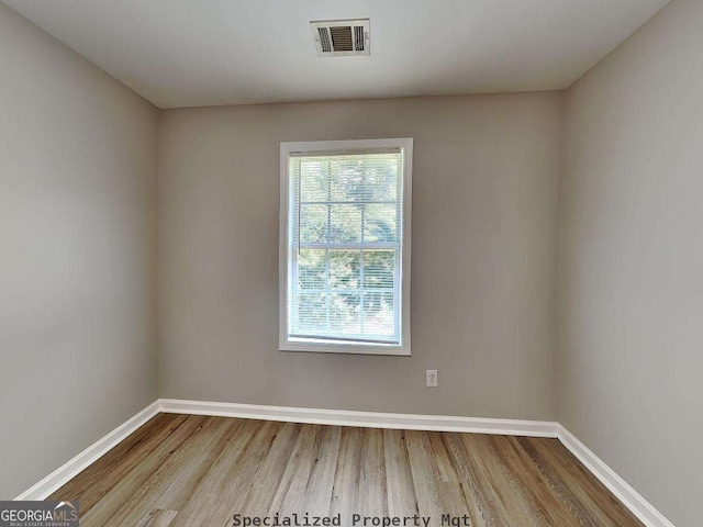 spare room featuring wood finished floors, visible vents, and baseboards