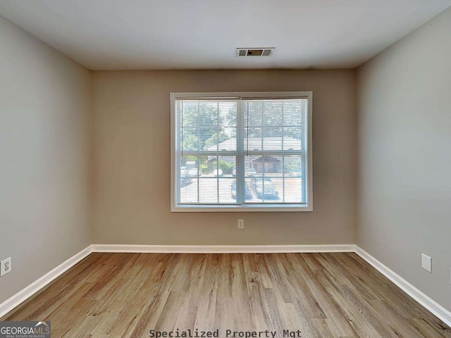 empty room featuring wood finished floors, visible vents, and baseboards