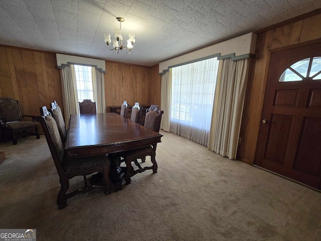 dining area featuring light carpet, a notable chandelier, and wood walls