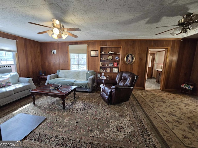 living room featuring wood walls, a wealth of natural light, and a ceiling fan